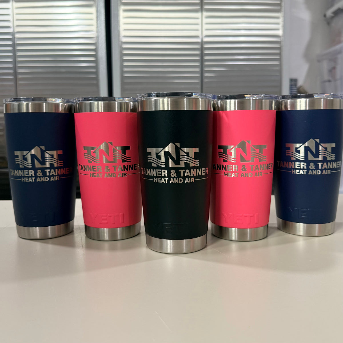 HVAC company logo laser engraved on five YETI Rambler 20 oz Tumblers in Navy, Tropical Pink and Black