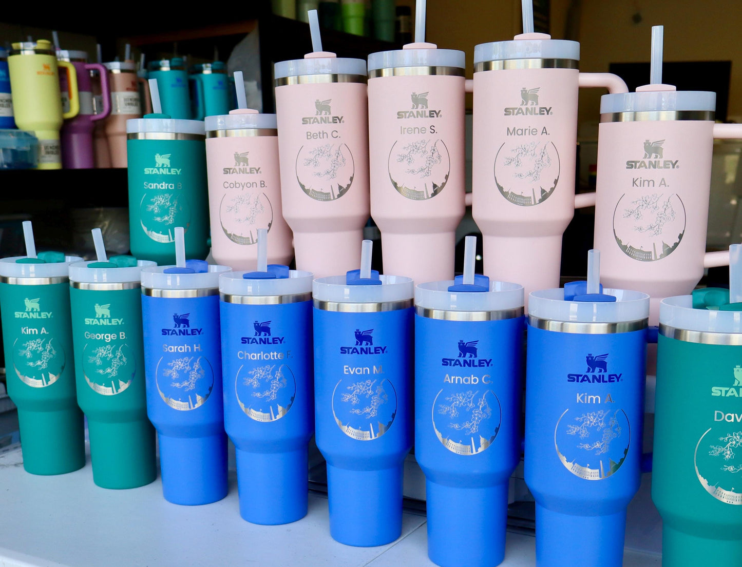 A company order of engraved Stanley Quenchers in pink, teal and blue, each with the company logo and an employee name